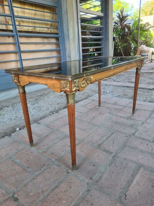 Mesa ratona de estilo Luis XVI con detalles en bronce pulido y tapa de vidrio superior.